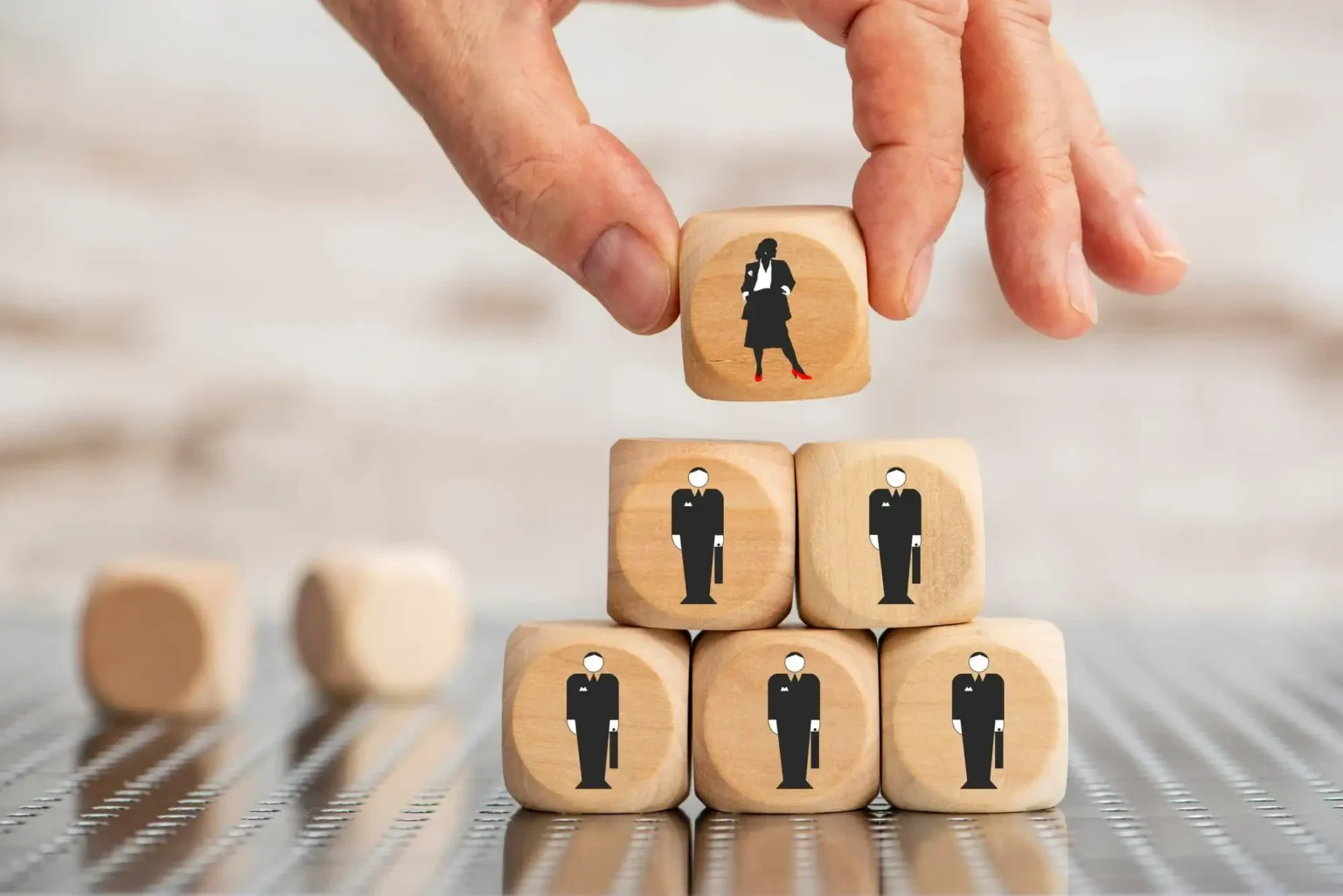 Une main place un cube représentant une femme en haut d’une pyramide de cubes illustrant des hommes en costume, symbolisant l’accès des femmes à des postes de leadership et l’égalité professionnelle.