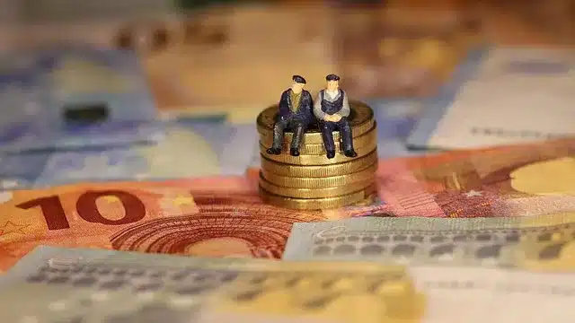 Deux figurines représentant des retraités assis sur une pile de pièces, symbolisant les enjeux financiers des retraites des agents publics territoriaux dans un contexte de déficit croissant de la CNRACL.