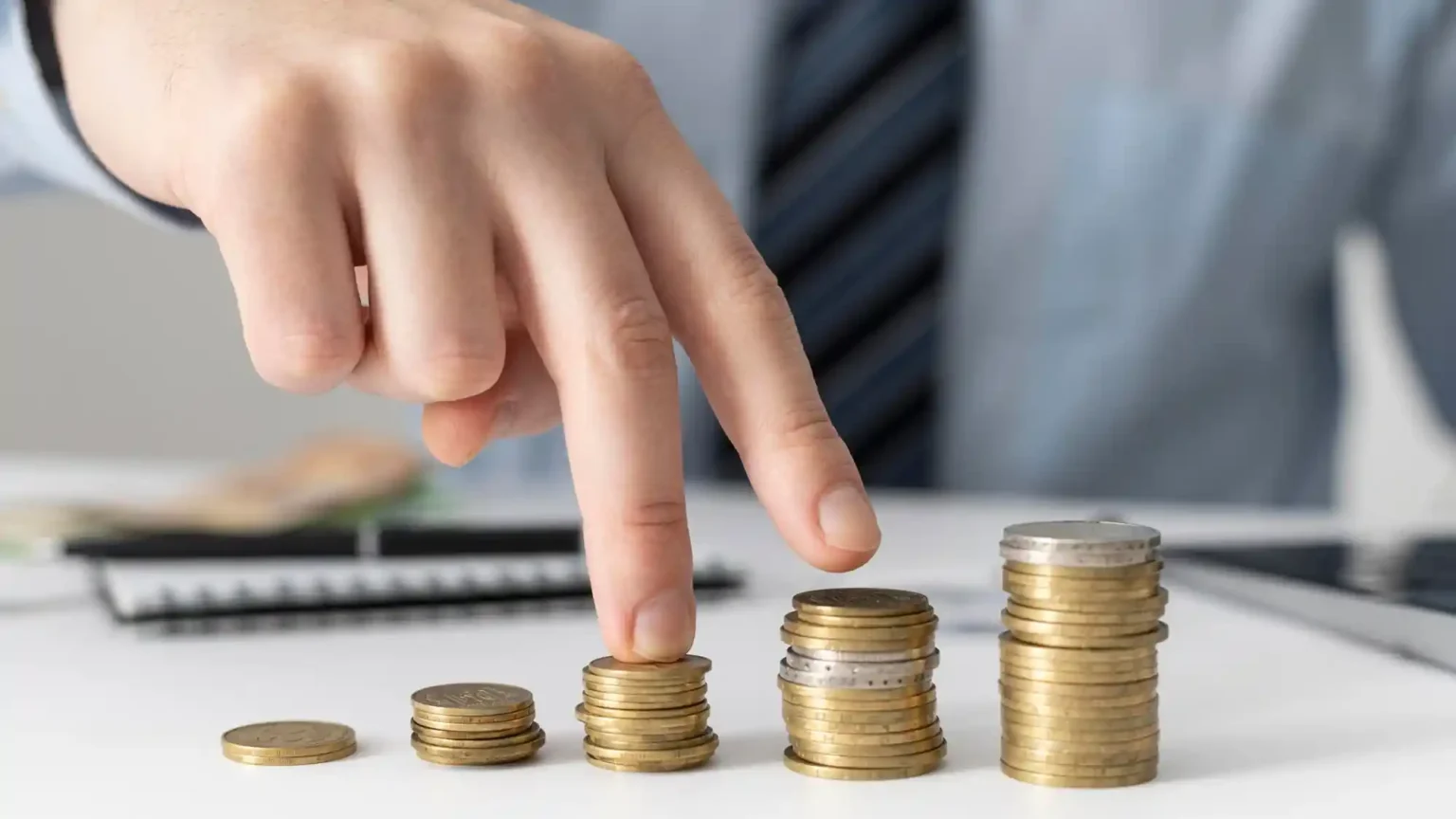 Main mimant une montée progressive sur des piles de pièces de monnaie, symbolisant la revalorisation salariale, les revendications sur le pouvoir d’achat et la lutte contre la vision comptable des agents publics .